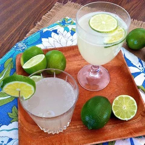 Glasses of homemade lime nectar on a wooden table with limes