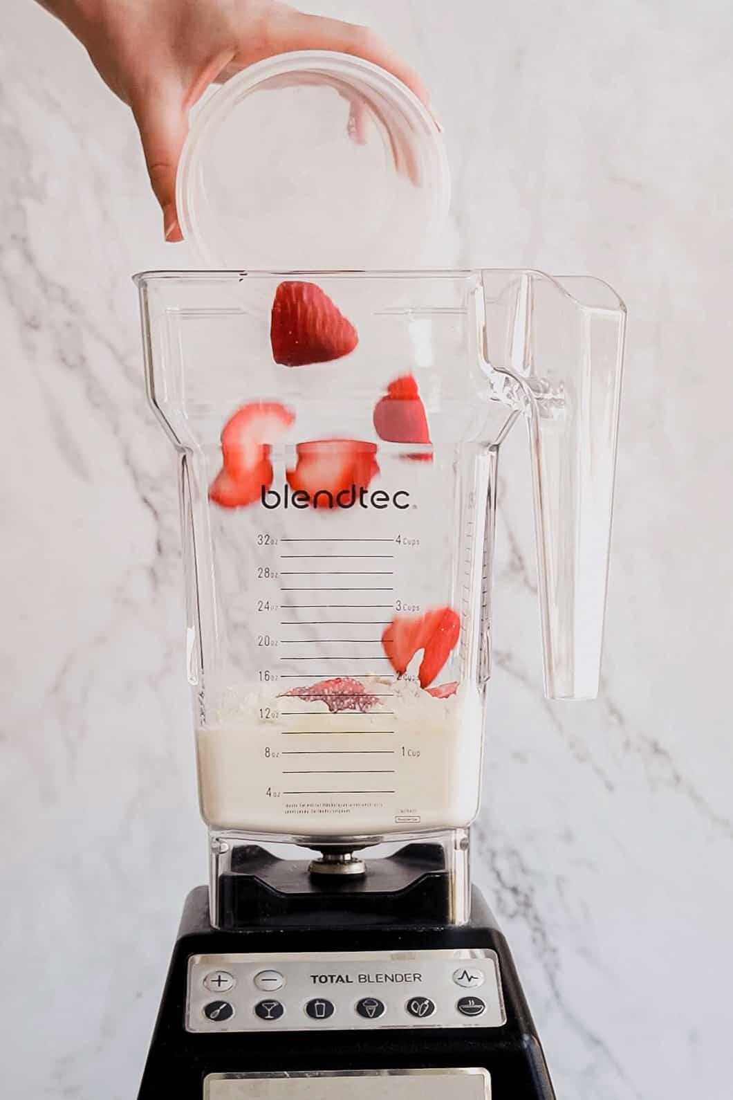 a hand adding spinach to a blender with strawberries and lemon