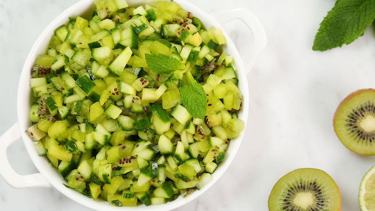 person tossing cucumber kiwi salsa salad in a bowl