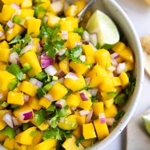 a close-up shot of a bowl of Coriander Crush Mango Salsa with a spoon scooping it up