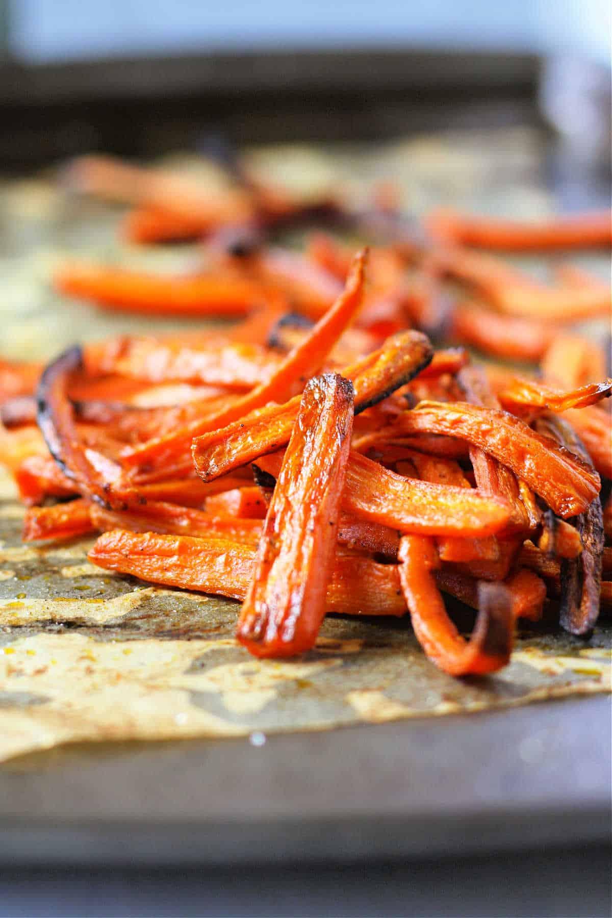 Close-up of roasted carrot fries being taken out of the oven, golden brown and slightly caramelized