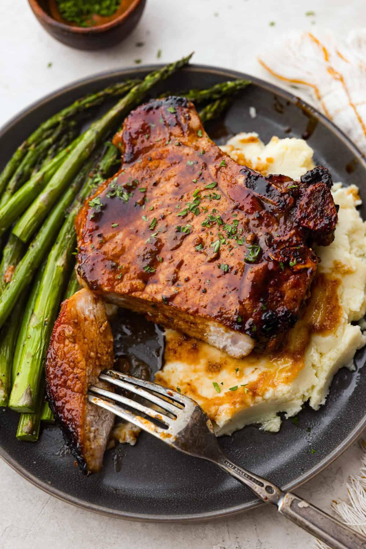 bourbon glazed pork chops plated with mashed sweet potatoes and asparagus