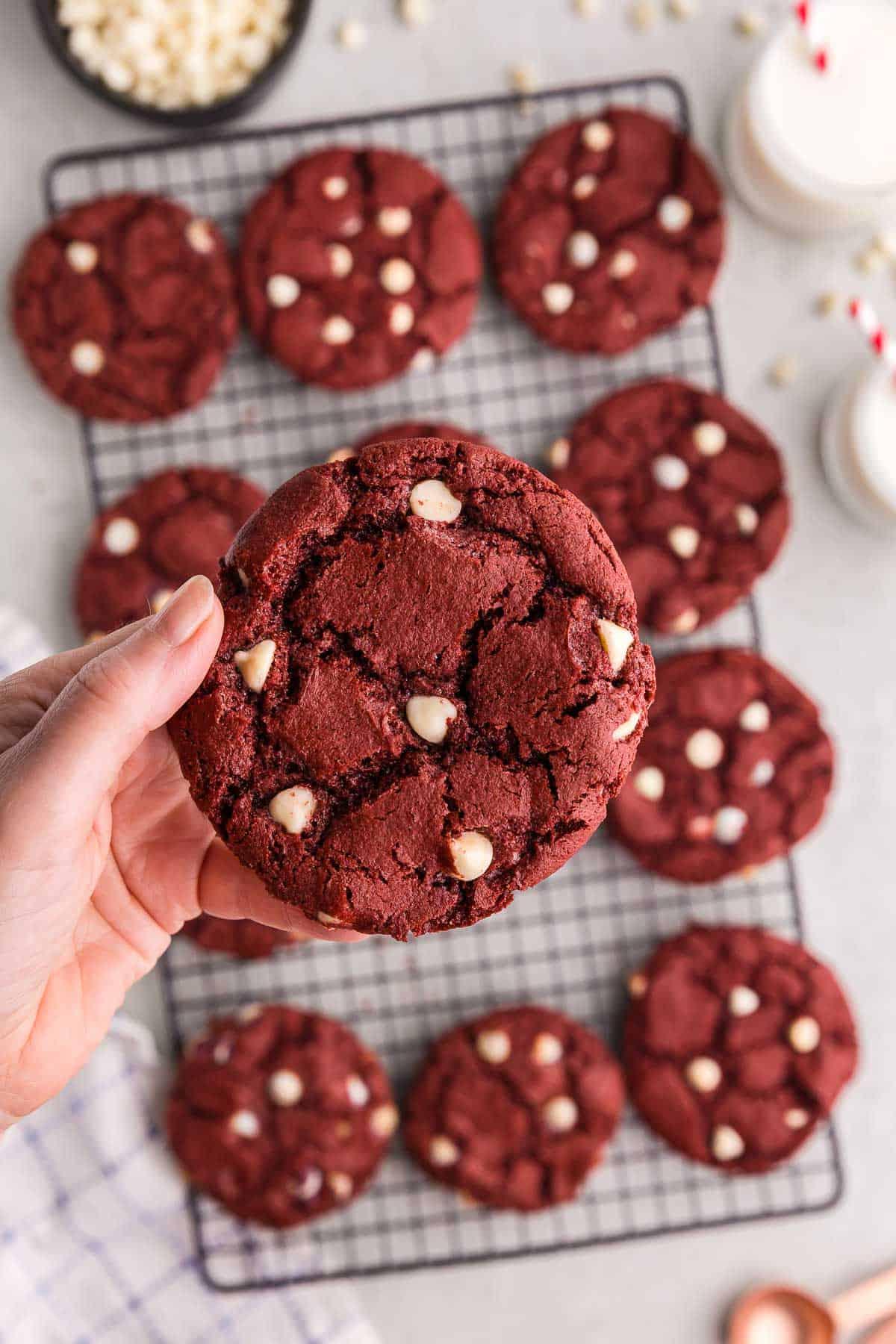 Close-up of baked red velvet swirl cookies on a cooling rack, some with a bite taken out, showing the intricate red and white pattern.