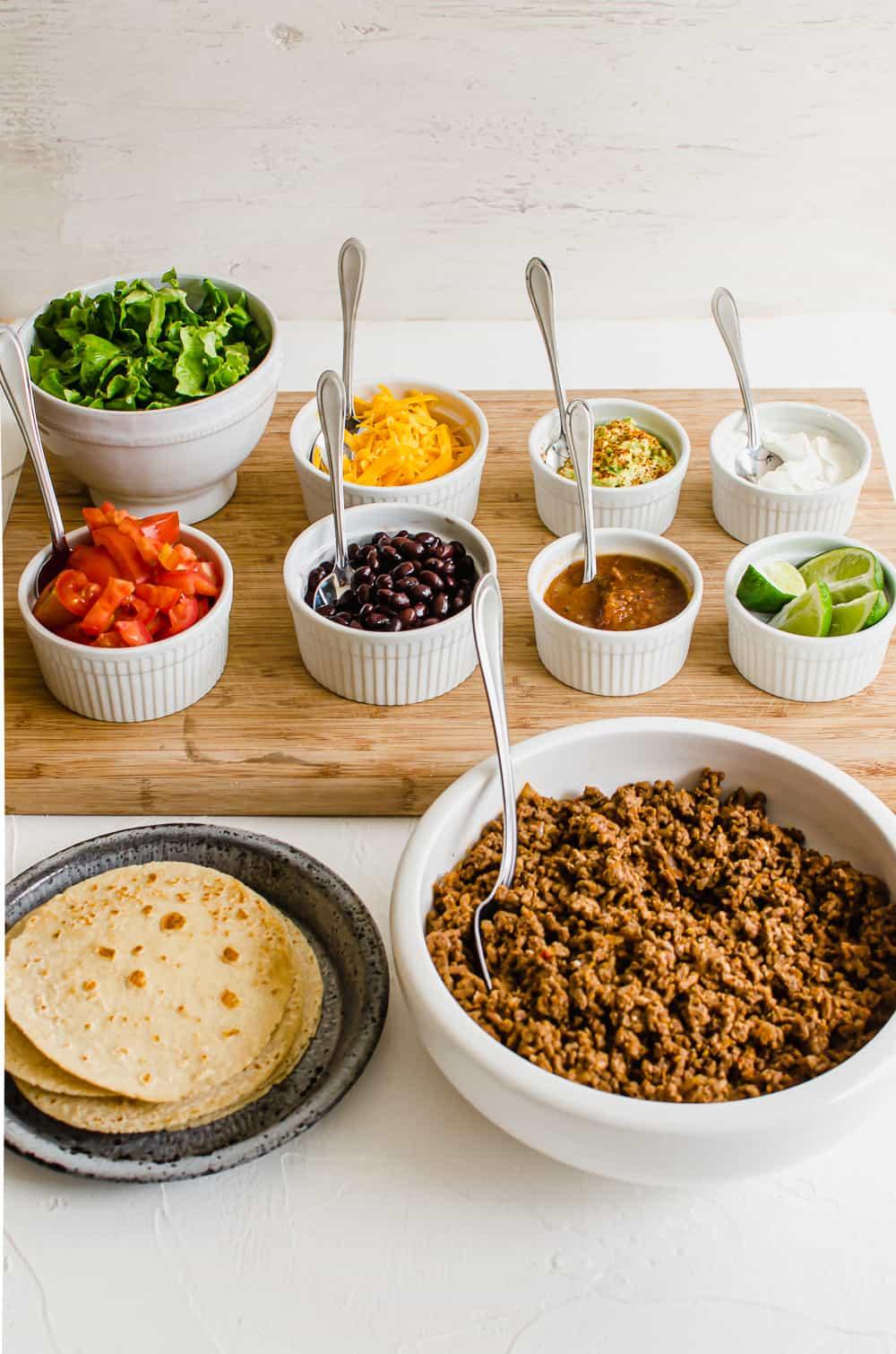 Various taco toppings arranged on a table, including avocado, salsa, Greek yogurt, and cotija cheese