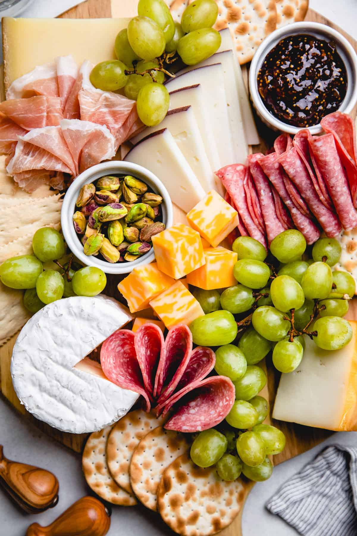 artisitic display of cheeses, crackers, fruits, and meats on a cheese platter