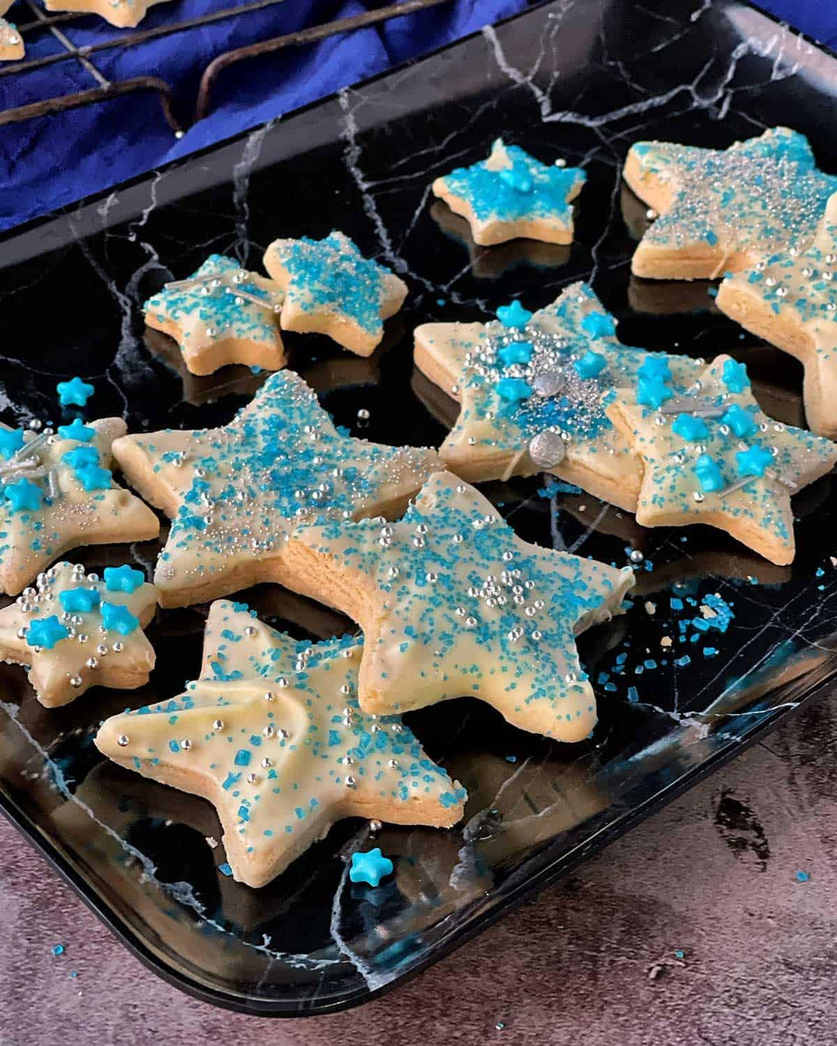 star-shaped shortbread cookies with edible glitter and blue food coloring, arranged on a sandy surface with seashells