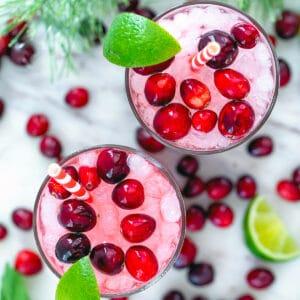 Overhead shot of a table with several glasses of cranberry lassi, garnished with cranberries and mint.