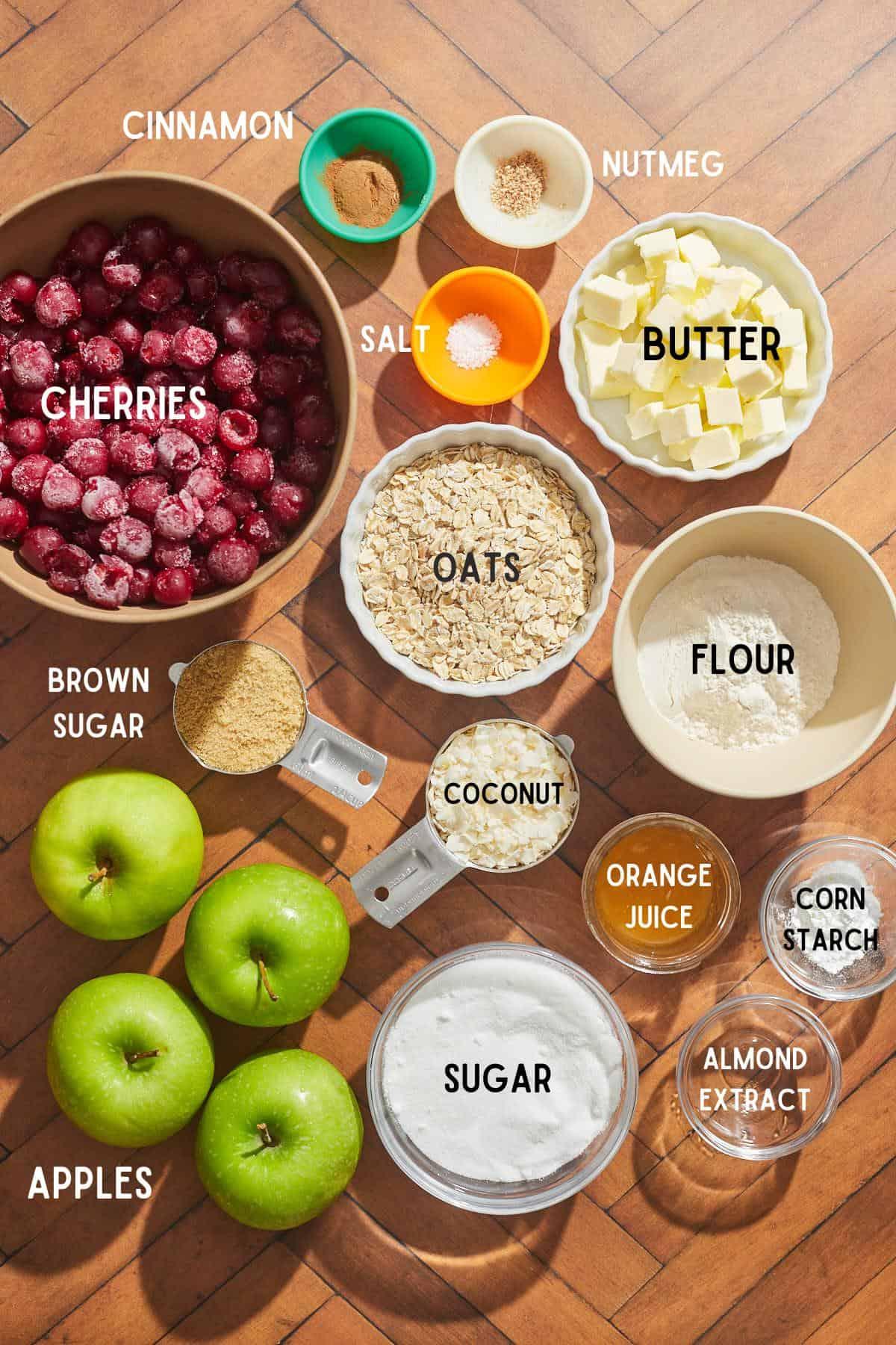 ingredients for cherry almond pear crisp arranged on a wooden table, including cherries, pears, almonds, flour, butter, and spices