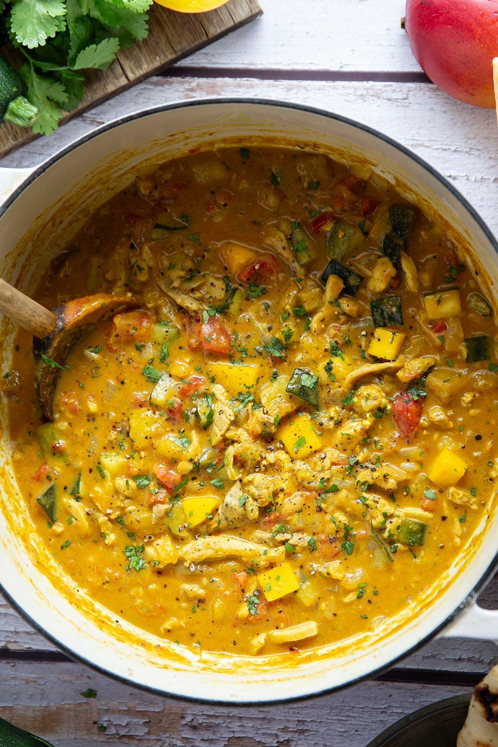 Close-up shot of chicken and vegetables simmering in a creamy curry sauce in a pot