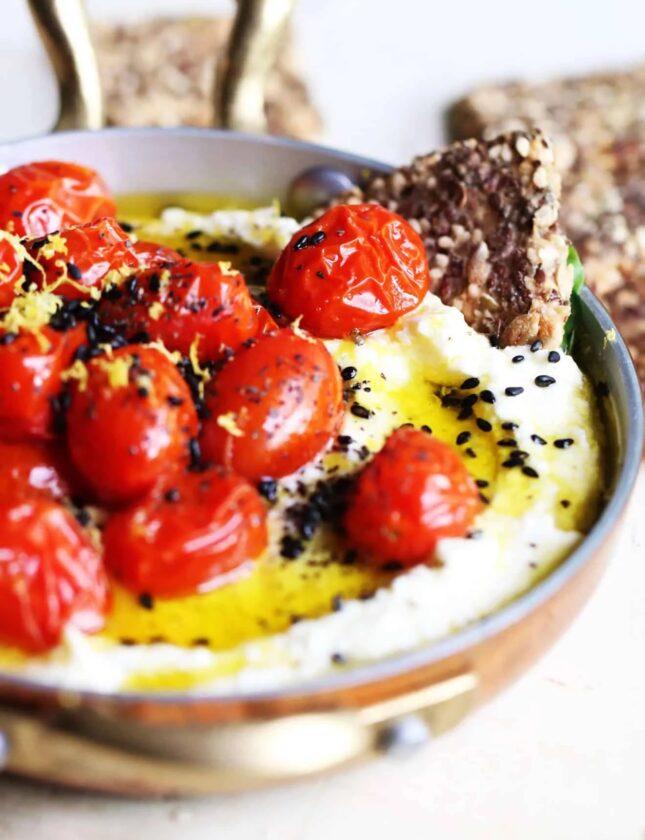 woman preparing whipped feta dip with roasted cherry tomatoes in a bright kitchen