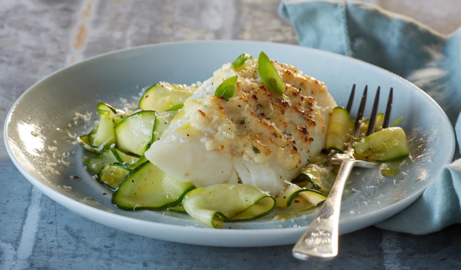 grilled cod and zucchini on a plate, garnished with fresh herbs