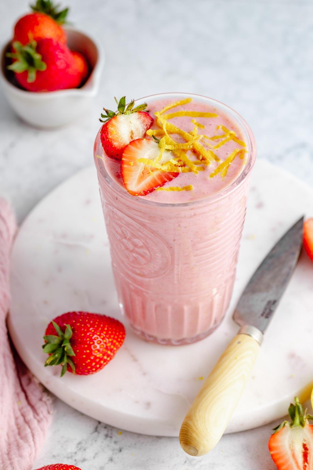 close up of a lemon strawberry smoothie in a glass with fresh strawberries and lemon slices around it