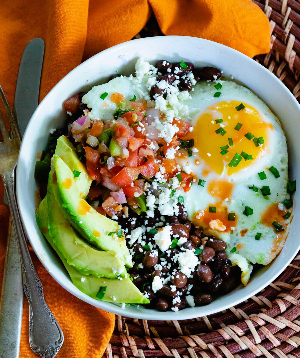 Vibrant Southwest breakfast burrito bowl with a fried egg and green chile, rustic wooden table
