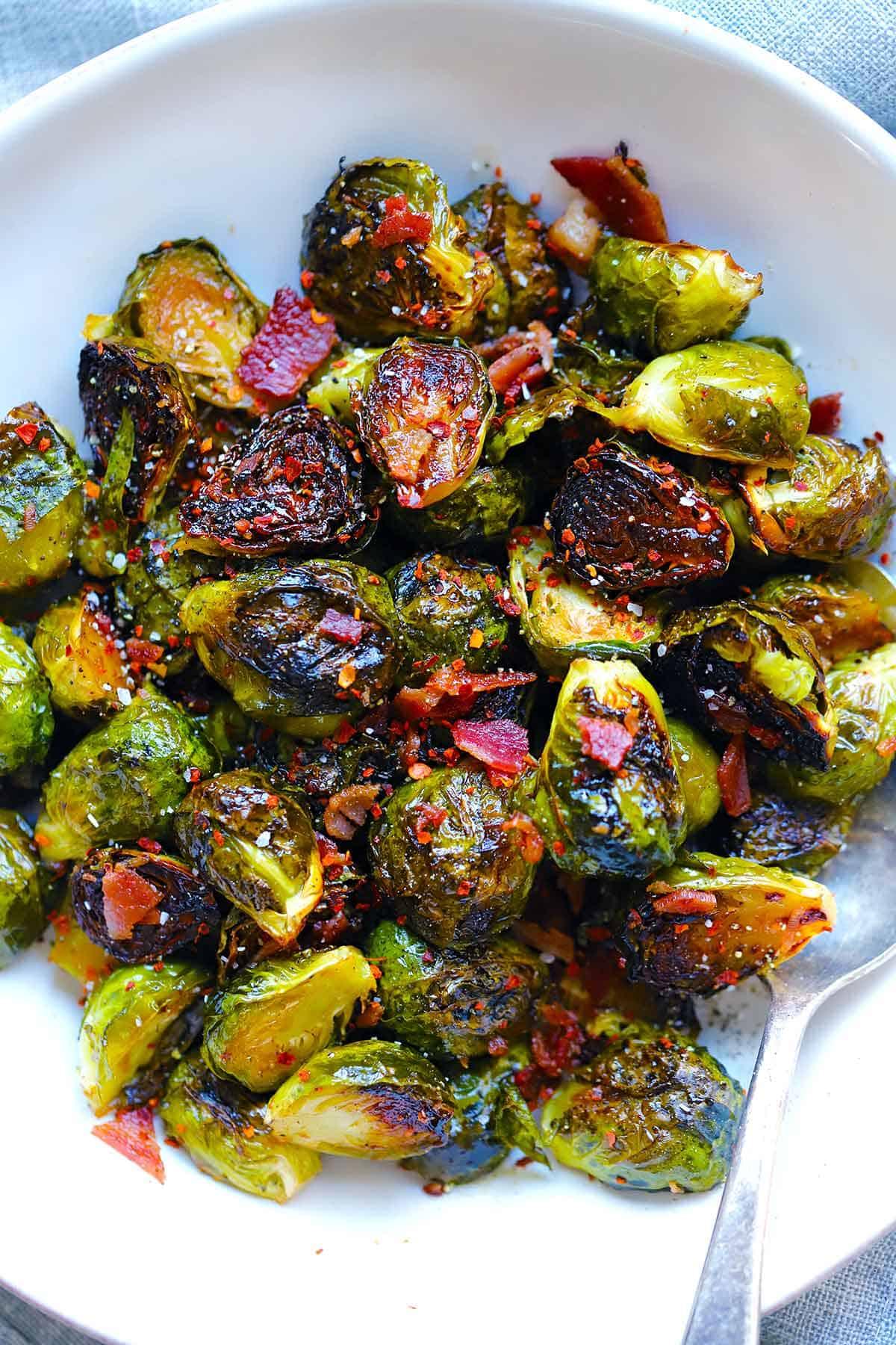 zucchini and brussels sprouts being tossed in a bowl with bacon and maple syrup