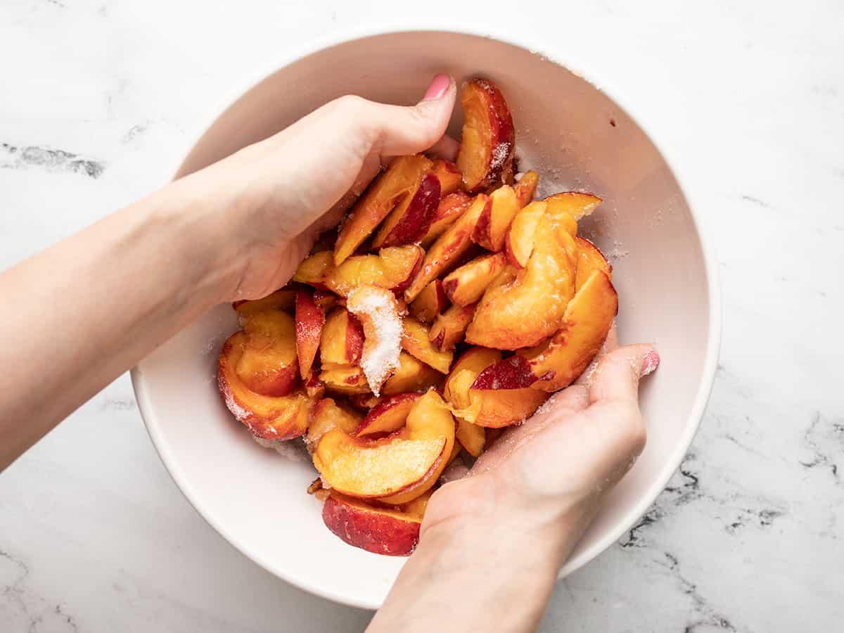 close-up shot of sliced peaches tossed with sugar and almond extract in a bowl