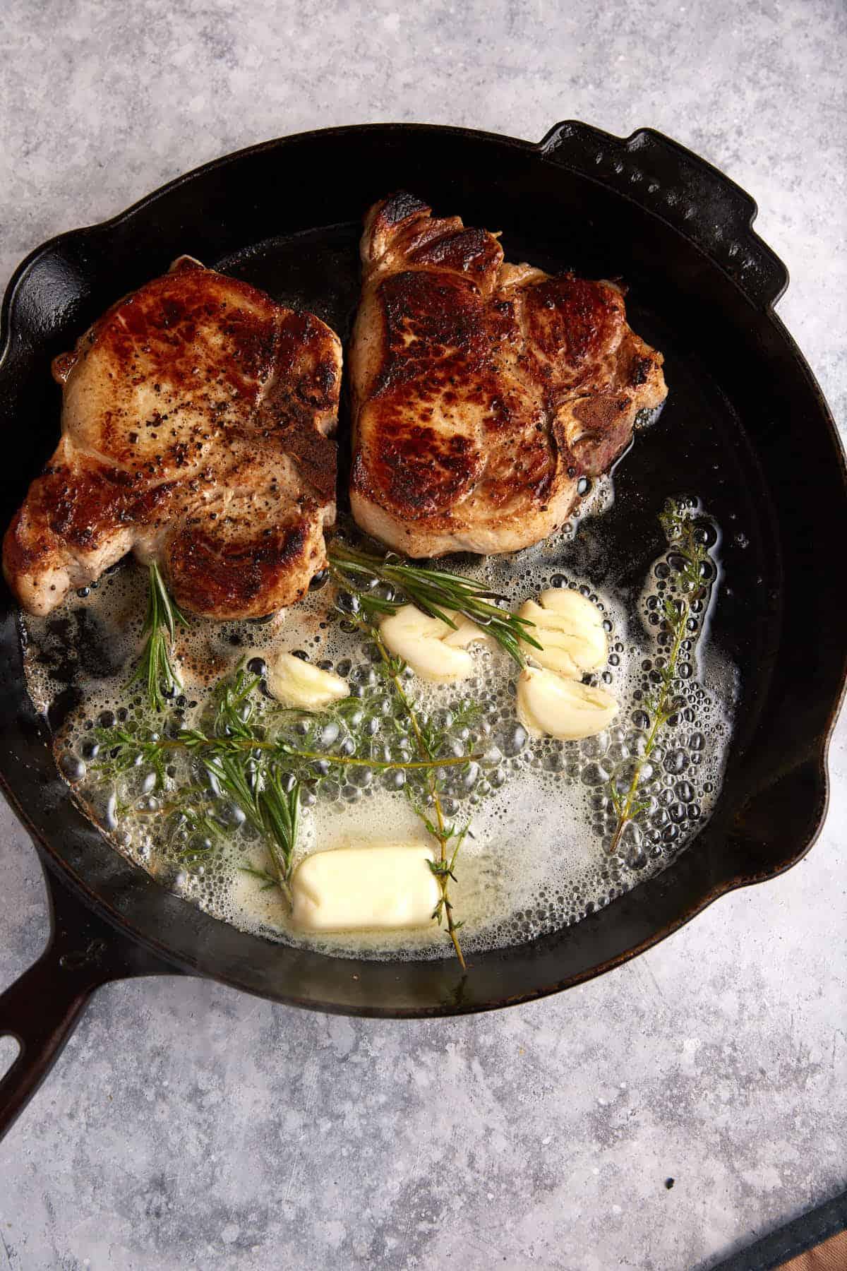 Pork chops searing in a cast iron skillet with black garlic paste.
