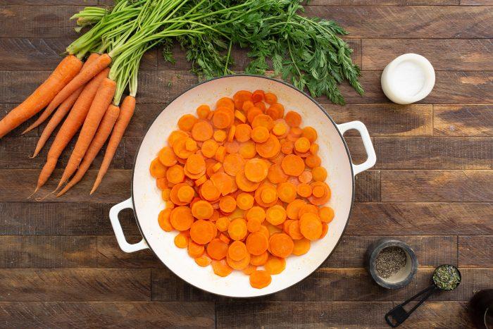 Carrots being tossed in a bowl with apple cider vinegar and spices