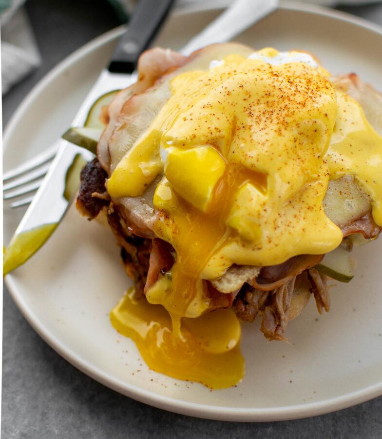 a perfectly assembled pork and bacon benedict with a knife cutting through the egg yolk