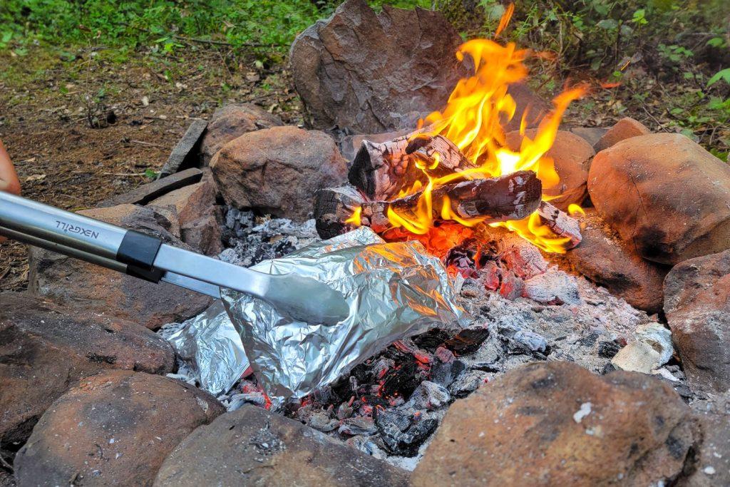 Hands placing foil packets onto a campfire