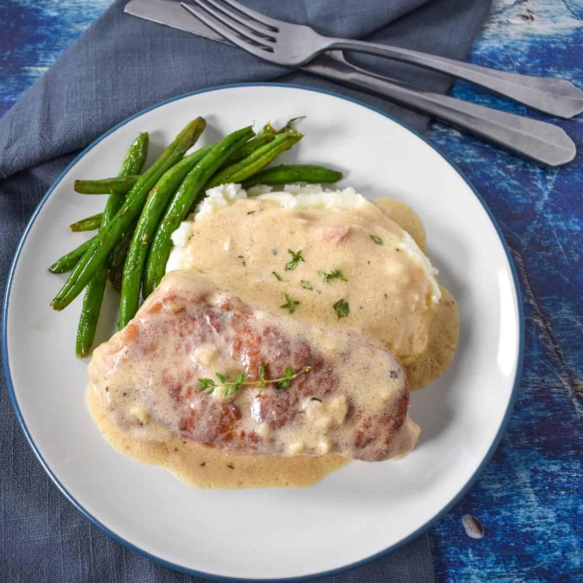 overhead shot of pork chops with creamy dill sauce being served on a plate with a side of mashed potatoes