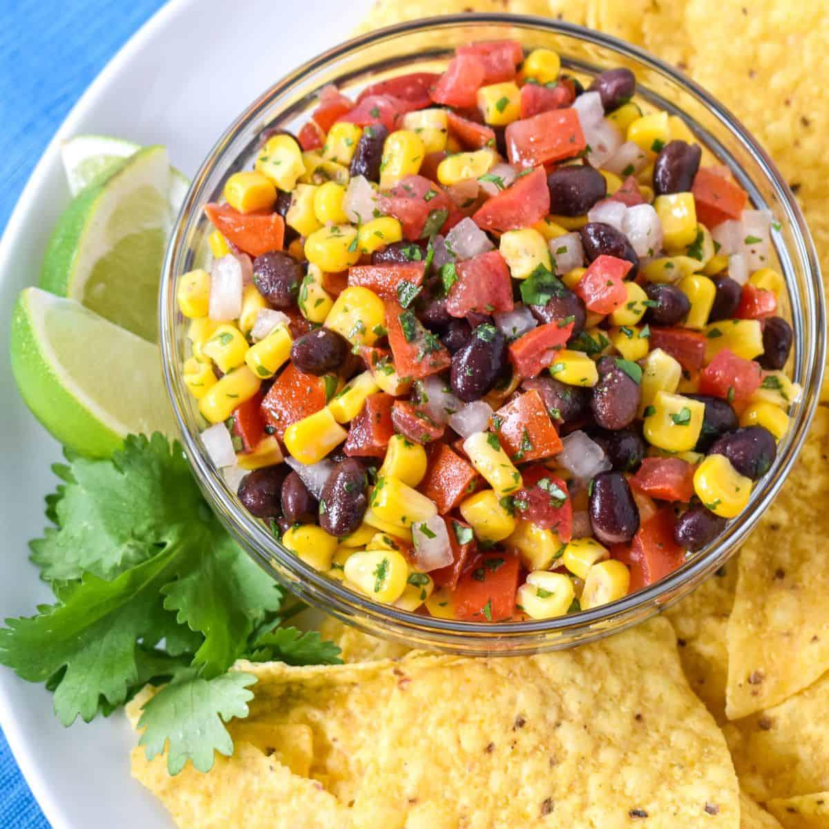 bowl of spicy black bean and corn salsa with lime wedges and tortilla chips