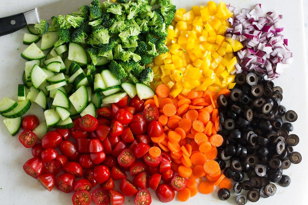 a variety of fresh vegetables being chopped for a pasta salad