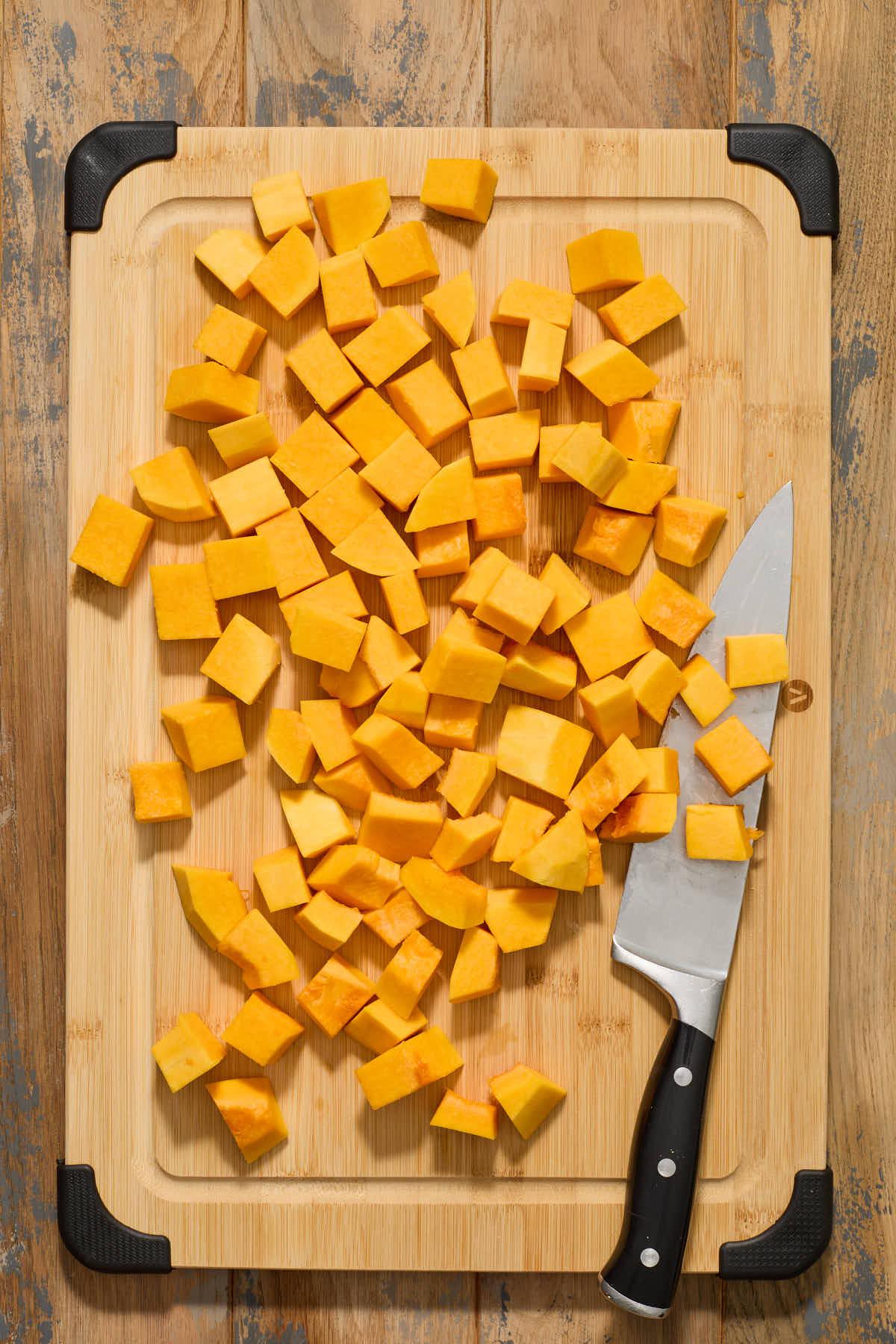 Butternut squash being cubed on a wooden cutting board