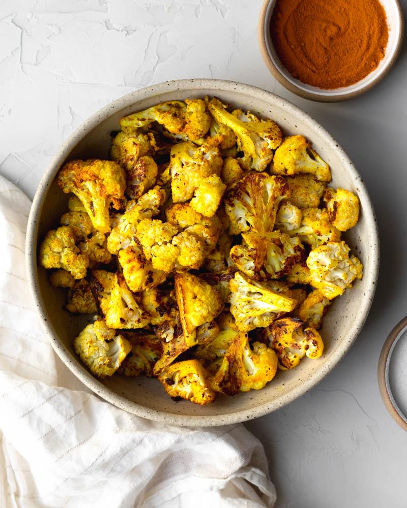 cauliflower florets being tossed in a bowl with spices