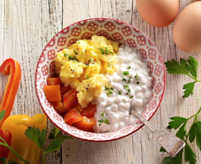 Cottage cheese being mixed with bell peppers and eggs in a bowl