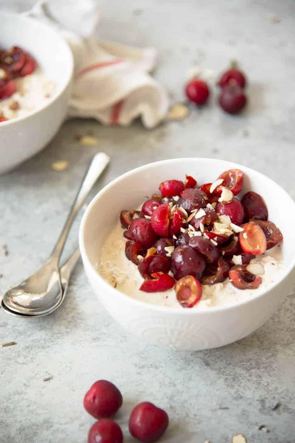 A bowl of Sleep Well Overnight Oats garnished with fresh cherries and a sprinkle of nutmeg, next to a lavender sprig.