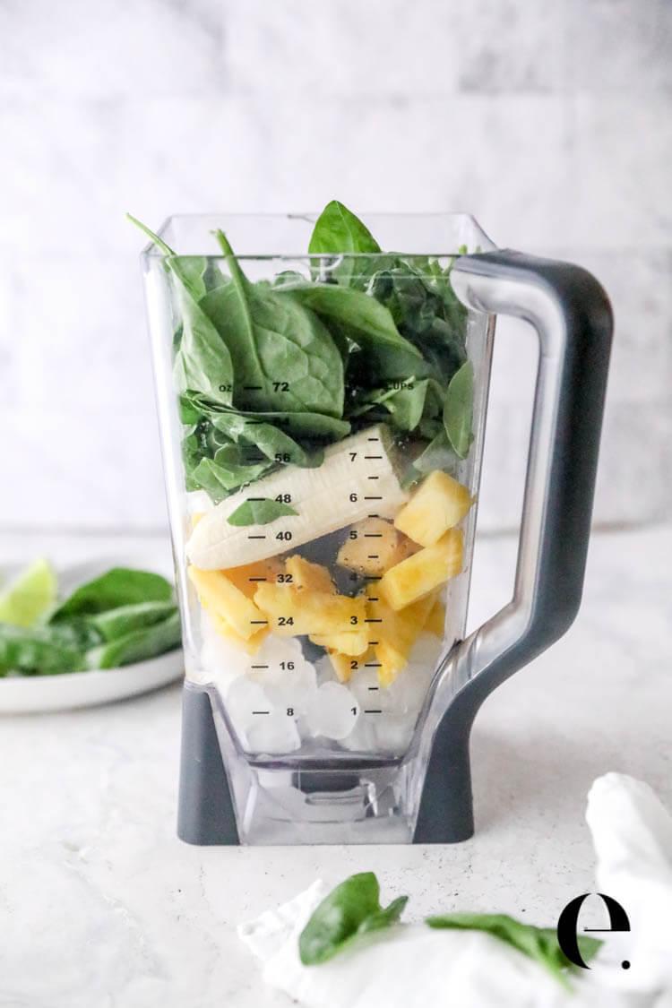 a person adding spinach to a blender with other smoothie ingredients