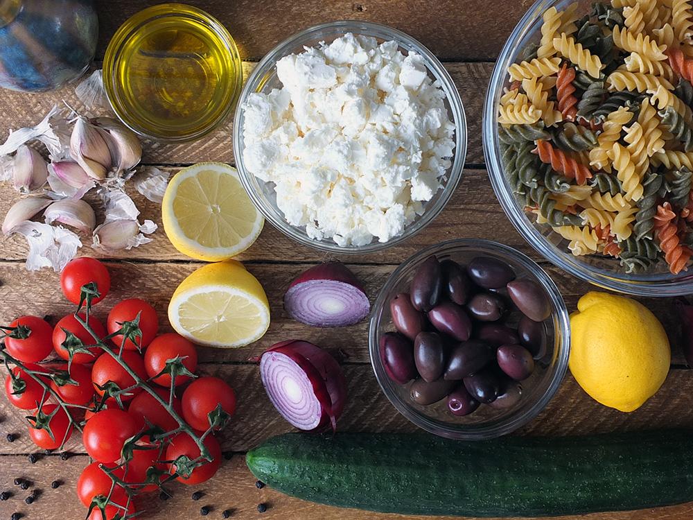 Ingredients for Greek pasta salad on a wooden table