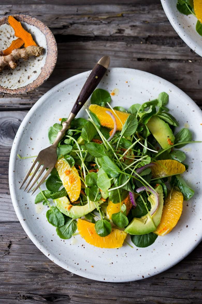 Close up of orange slices being arranged on top of a watercress salad