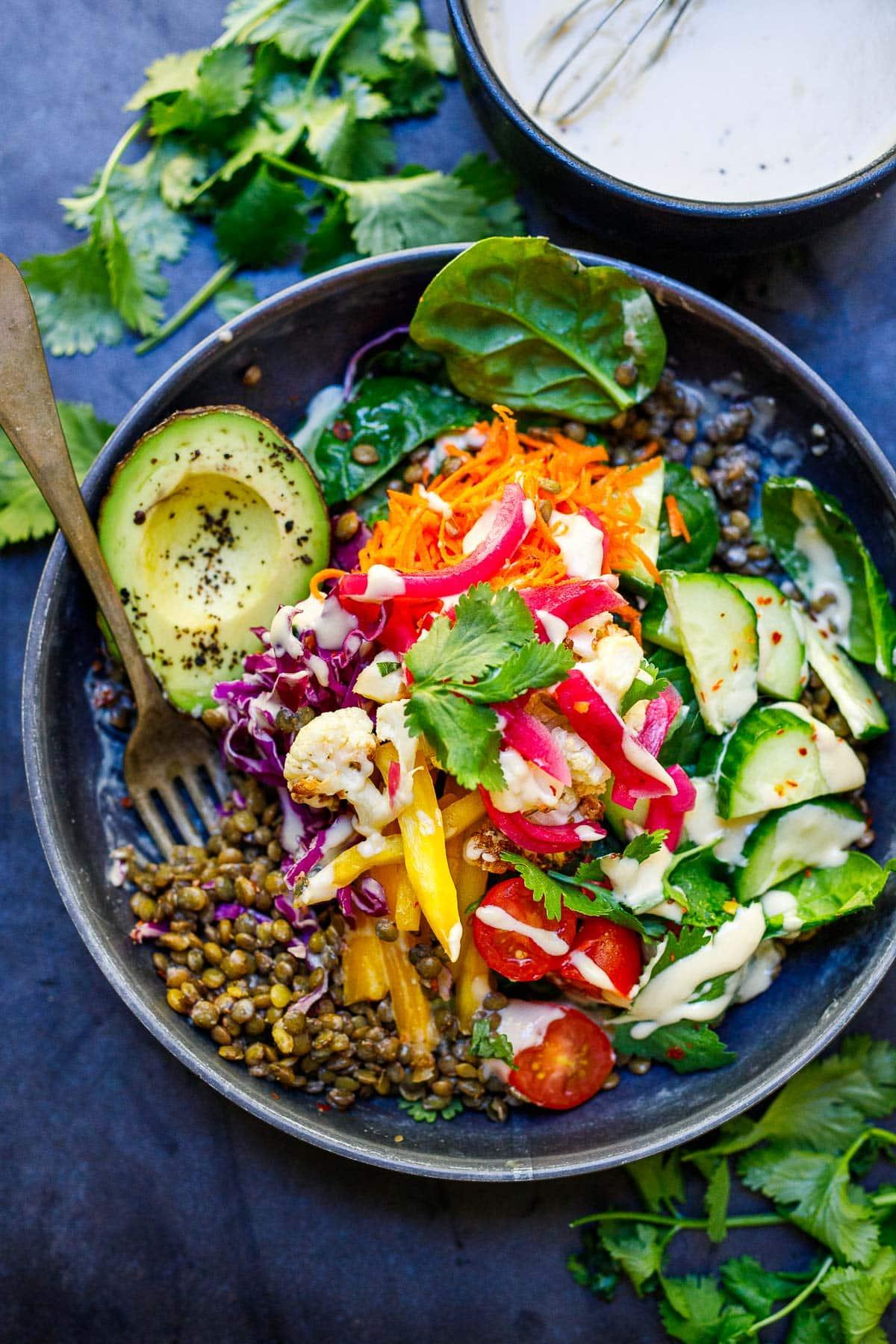 A bowl of lentil and roasted vegetable bowl drizzled with dressing and sprinkled with fresh herbs