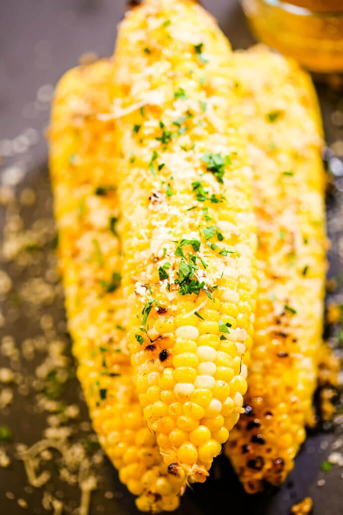 close up of grilled corn being brushed with garlic parmesan butter