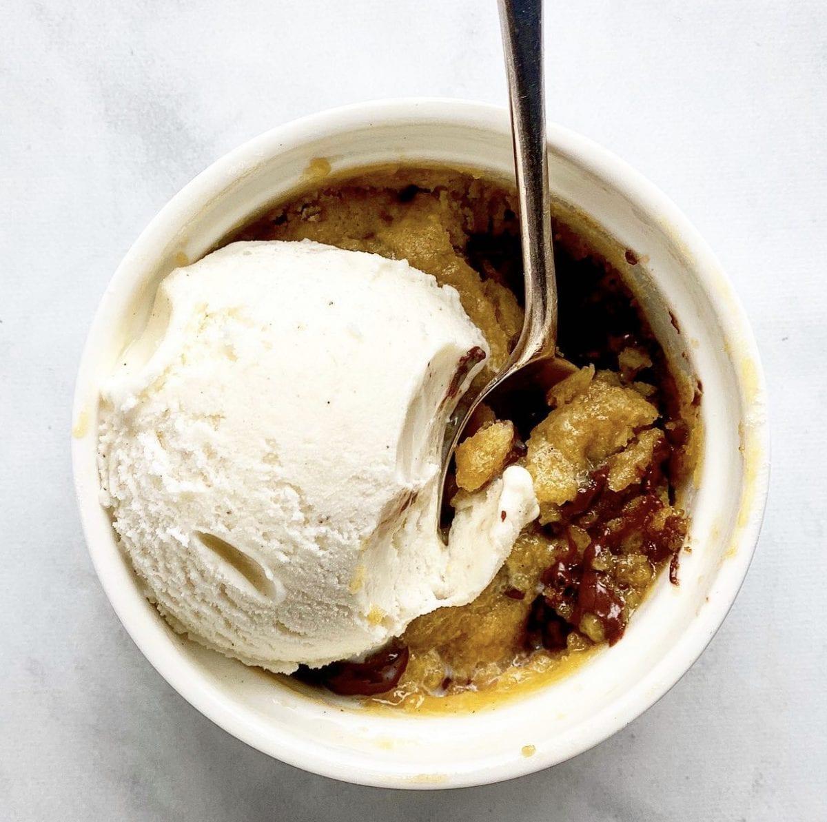 a spoon scooping a bite out of a chocolate chip cookie dough mug cake, revealing the gooey center