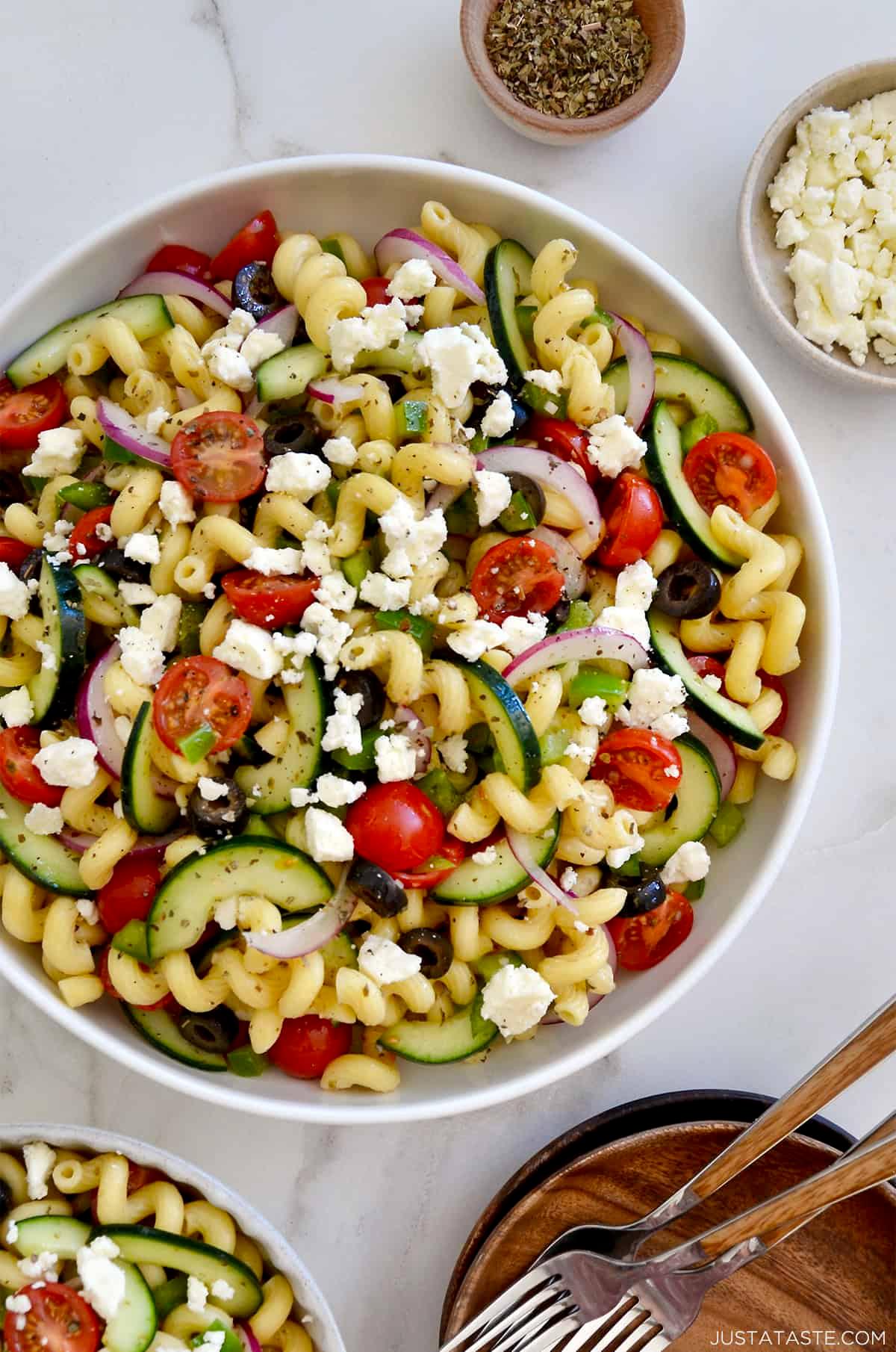 Greek pasta salad being tossed with dressing in a large bowl