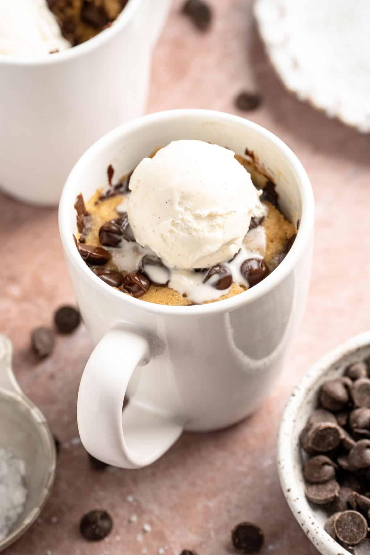 A chocolate chip cookie dough mug cake topped with a small scoop of vanilla ice cream and chocolate syrup