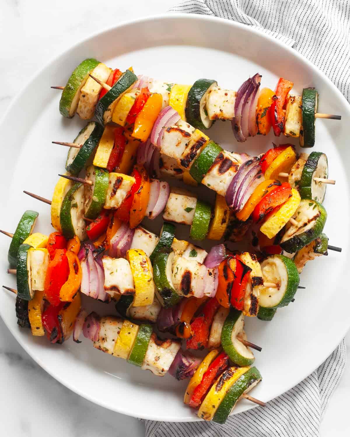 a person assembling grilled halloumi and vegetable skewers on a plate