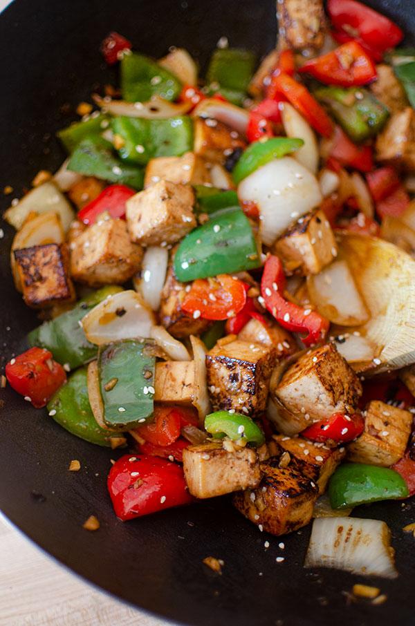 Tofu cubes being stir-fried in a wok with colorful bell peppers and onions