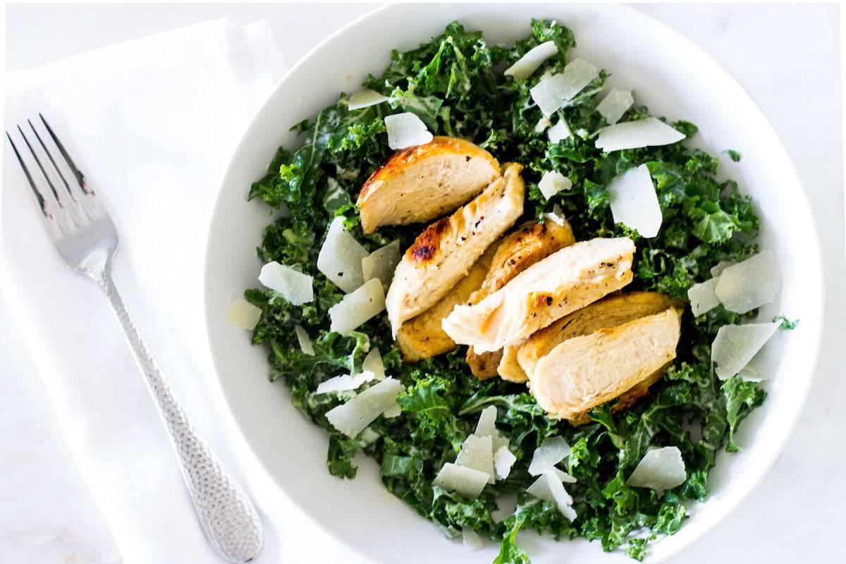 Overhead shot of someone preparing Kale Caesar Chicken Parmesan in a kitchen
