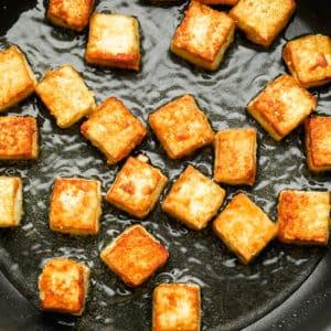 Close-up of tofu cubes being pan-fried in a skillet with watermelon pieces