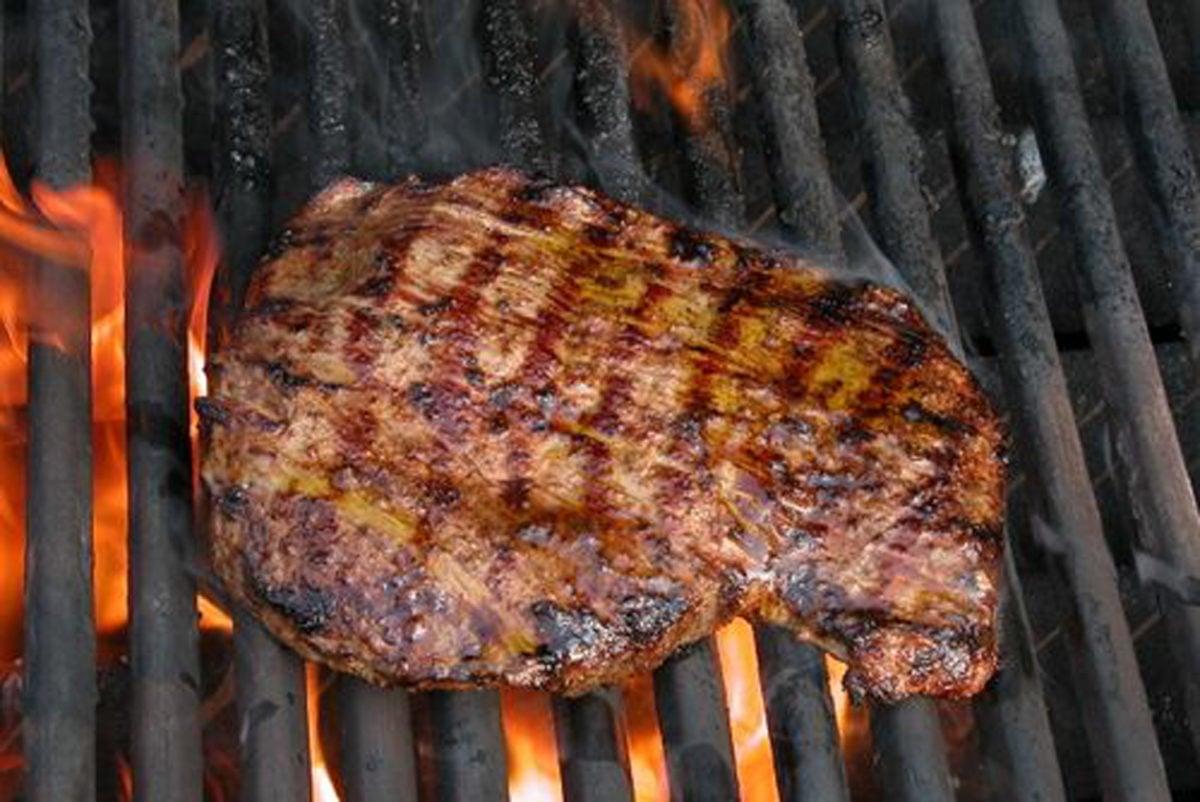 Close up of Apricot Dijon Flank Steak grilling on an outdoor grill