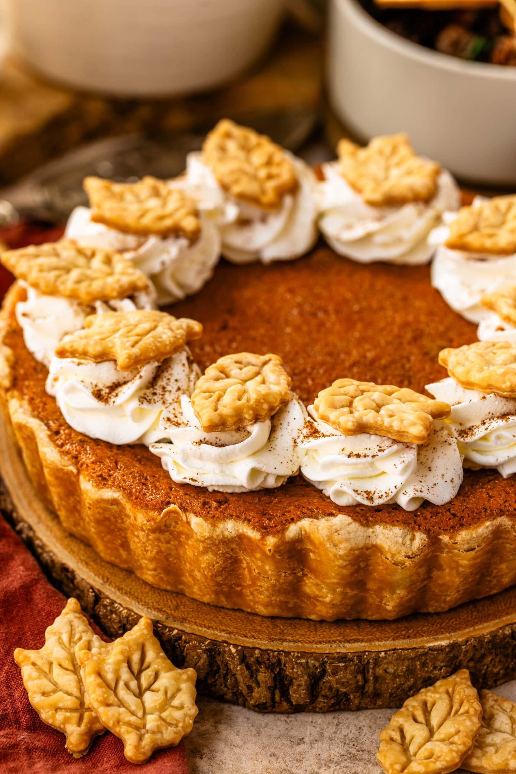 Homemade sweet potato pie with a golden crust and creamy filling, garnished with a dollop of whipped cream, on a wooden table with fall decorations