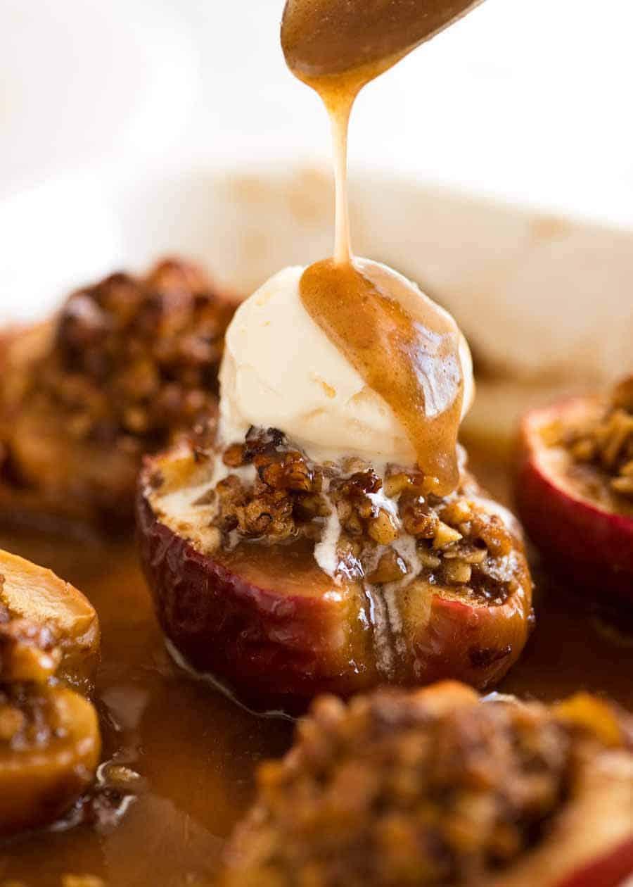 A close-up shot of a baked apple being drizzled with caramel sauce, showcasing its glistening texture.