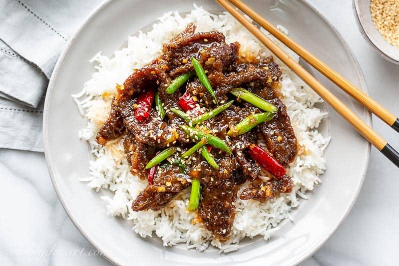 Overhead shot of a spicy beef stir-fry in a bowl, garnished with sesame seeds and green onions