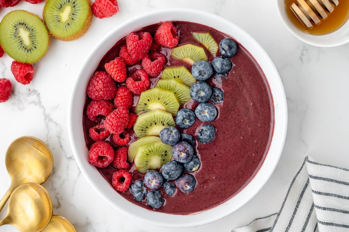 Overhead shot of a vibrant acai berry smoothie bowl topped with various fruits, nuts, and seeds