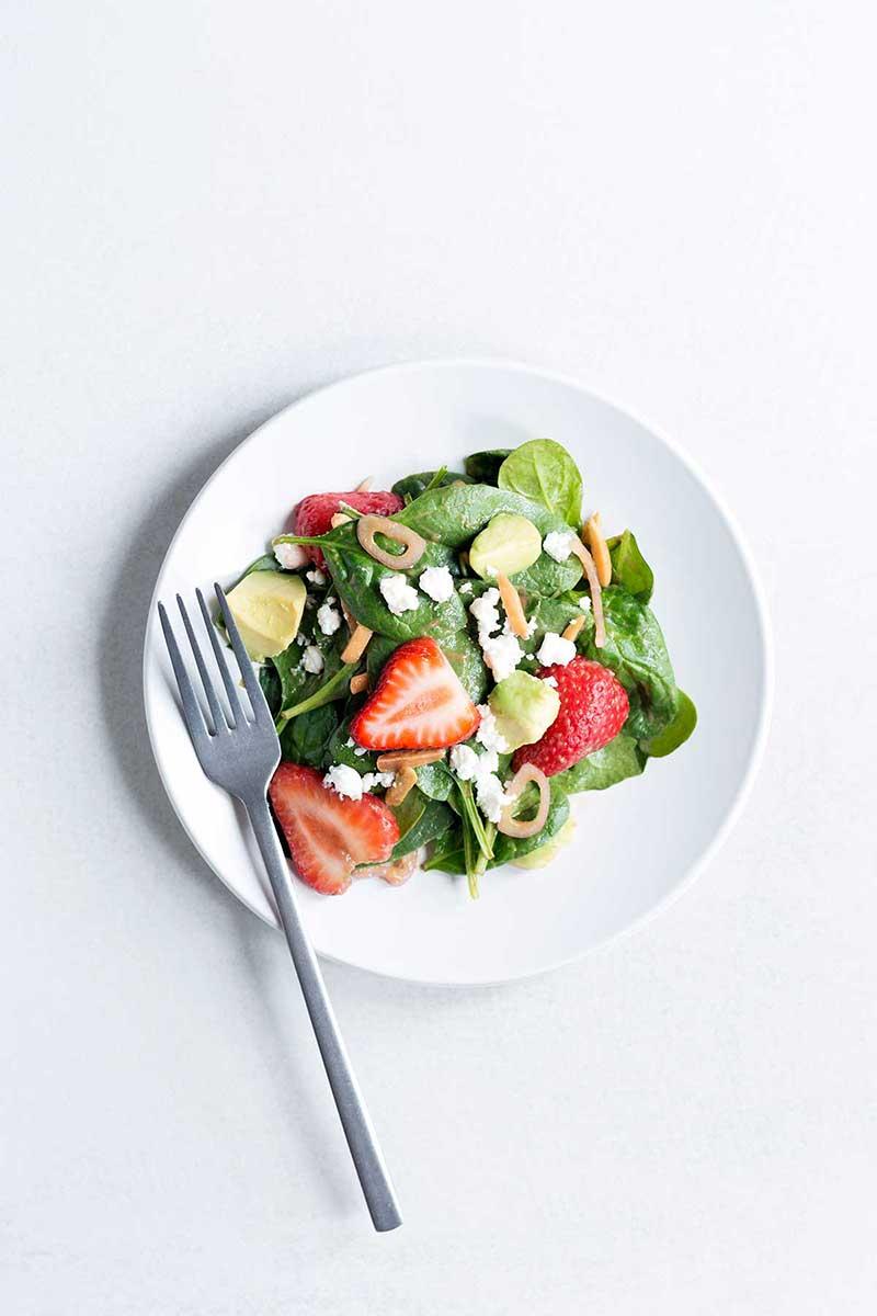 overhead shot of a vibrant strawberry spinach salad in a clear bowl