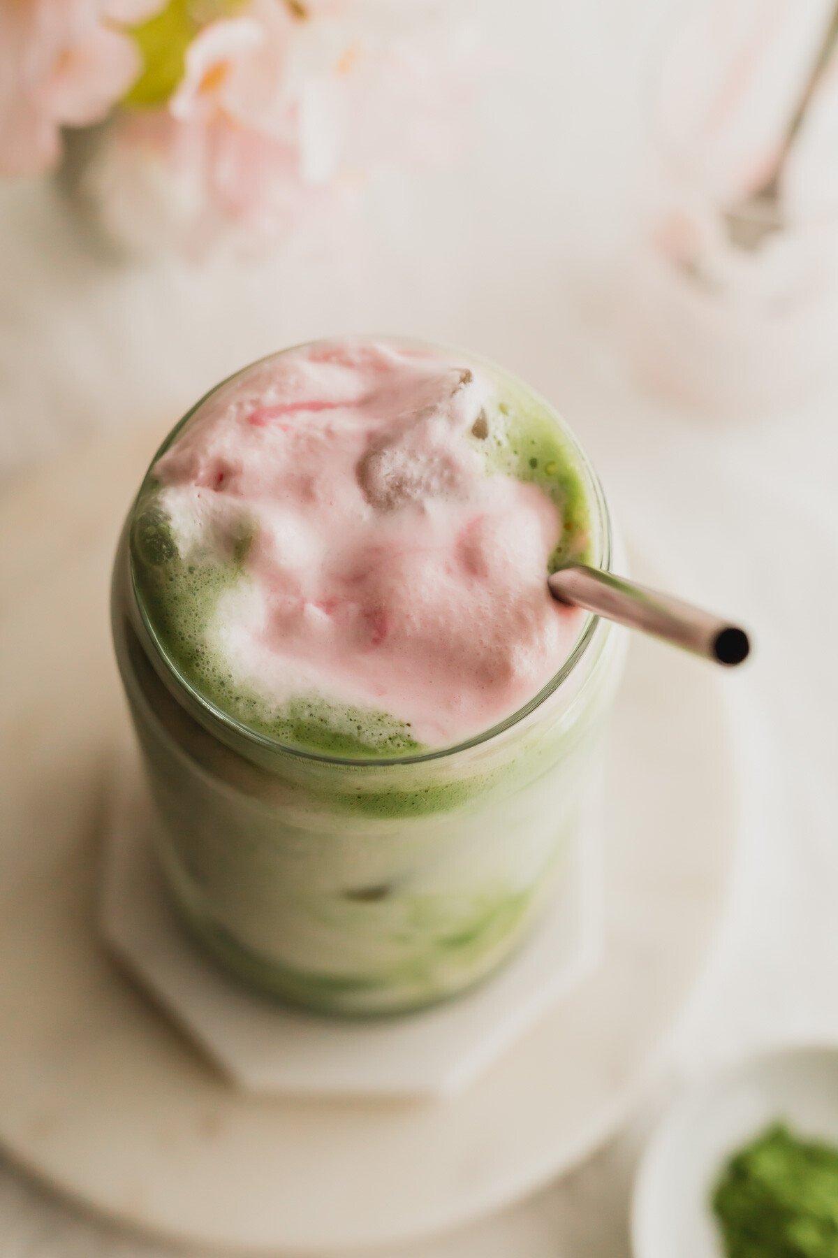 close up of frothy matcha cherry blossom latte in a glass mug