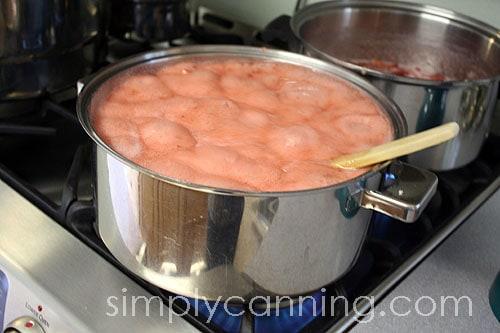 a person stirring strawberry and rhubarb jam in a large pot on the stove